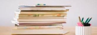 Photo représentant une pile de livres pro (avec des post-its) et un pot à craon posé à côté 